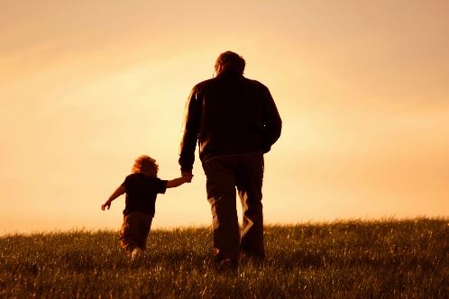 a man with paternity holds his child's hand and walks into the sunset